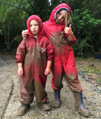 Two children covered in mud wearing Mud Mates NZ-made waterproof coveralls to keep their clothes clean and dry