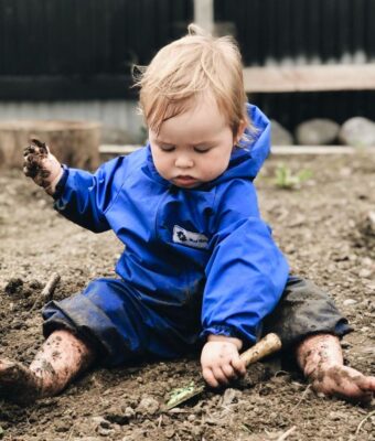 Young child playing in dirt, keeping clean and dry in her NZ-made waterproof coveralls in royal blue
