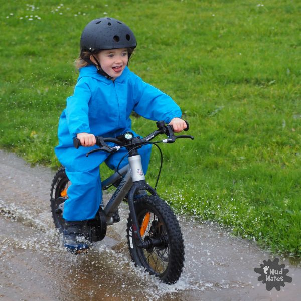 Fun & Free Kids Activities for the School Holidays - young girl riding her bike through a puddle of water, keeping dry in her Mud Mates coveralls