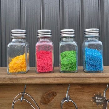 Homemade edible glitter in four glass shakers - yellow, red, green and blue - made from rice paper, water and food colouring