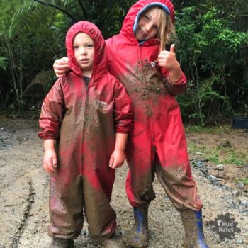 Two kids covered in mud showing the benefits of muddy play in Mud Mates red coveralls