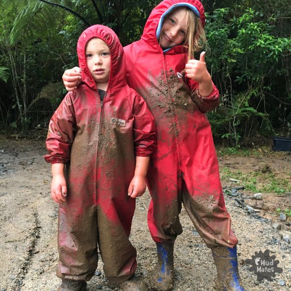 Two kids covered in mud showing the benefits of muddy play in Mud Mates red coveralls