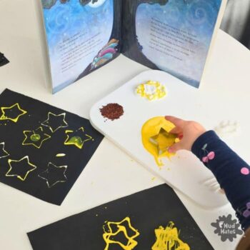 Girl stamping Matariki stars onto dark card with cookie cutters and paint alongside a Matariki book